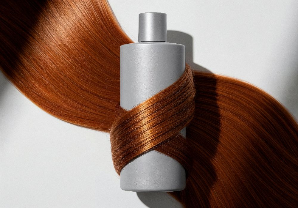 Пляшка засобу для догляду за волоссям, обгорнута гладким мідним волоссям — символ живлення та відновлення.