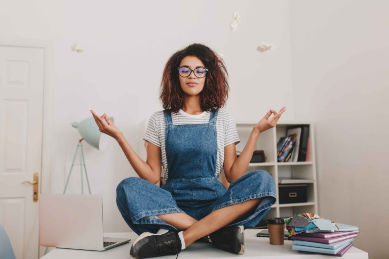 relaxed-young-woman-with-bronze-skin-sitting-lotus-pose-table-with-laptop-documents