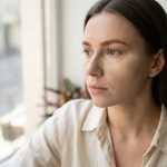 Задумлива молода жінка дивиться у вікно на місто.